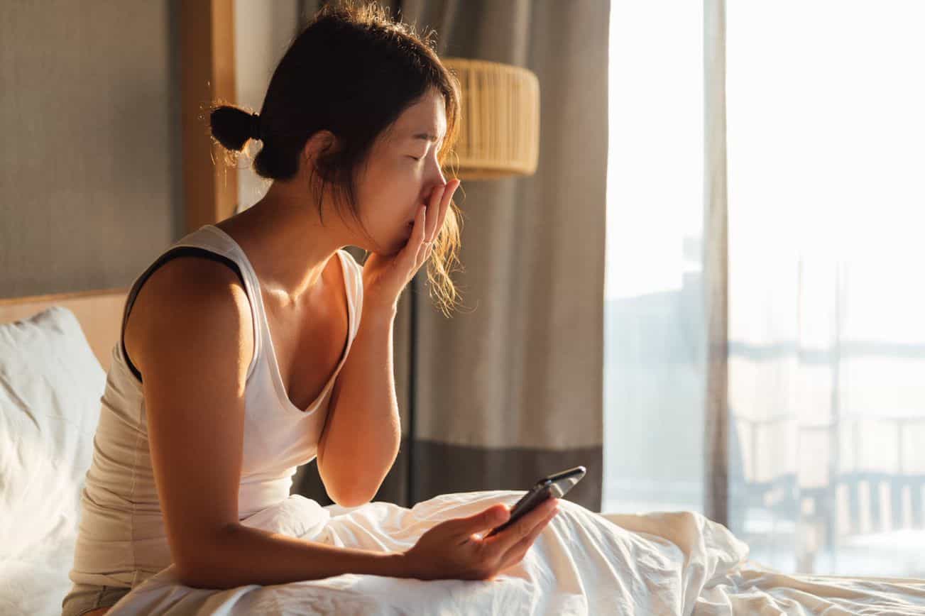 Women yawning in bed looking at her phone
